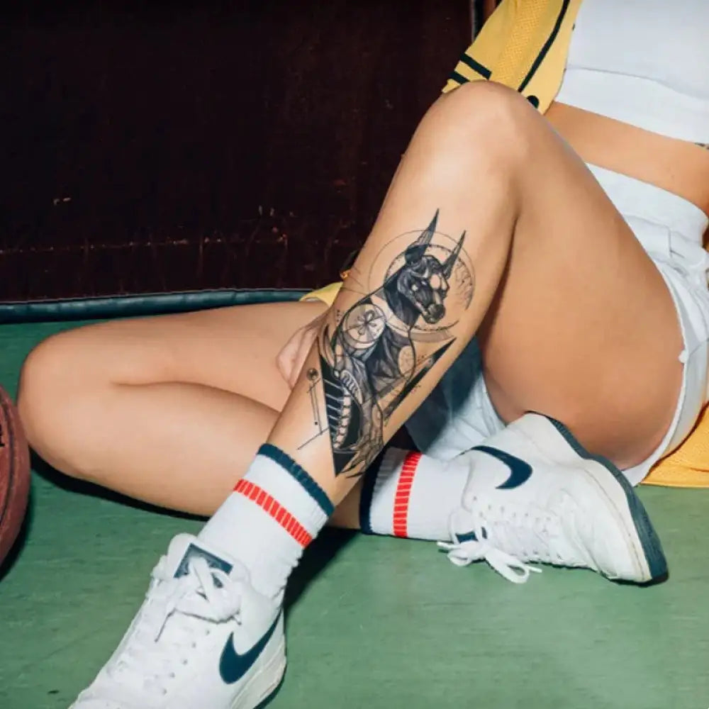 Person’s leg with an Anubis tattoo sticker, striped socks, and white Nike sneakers