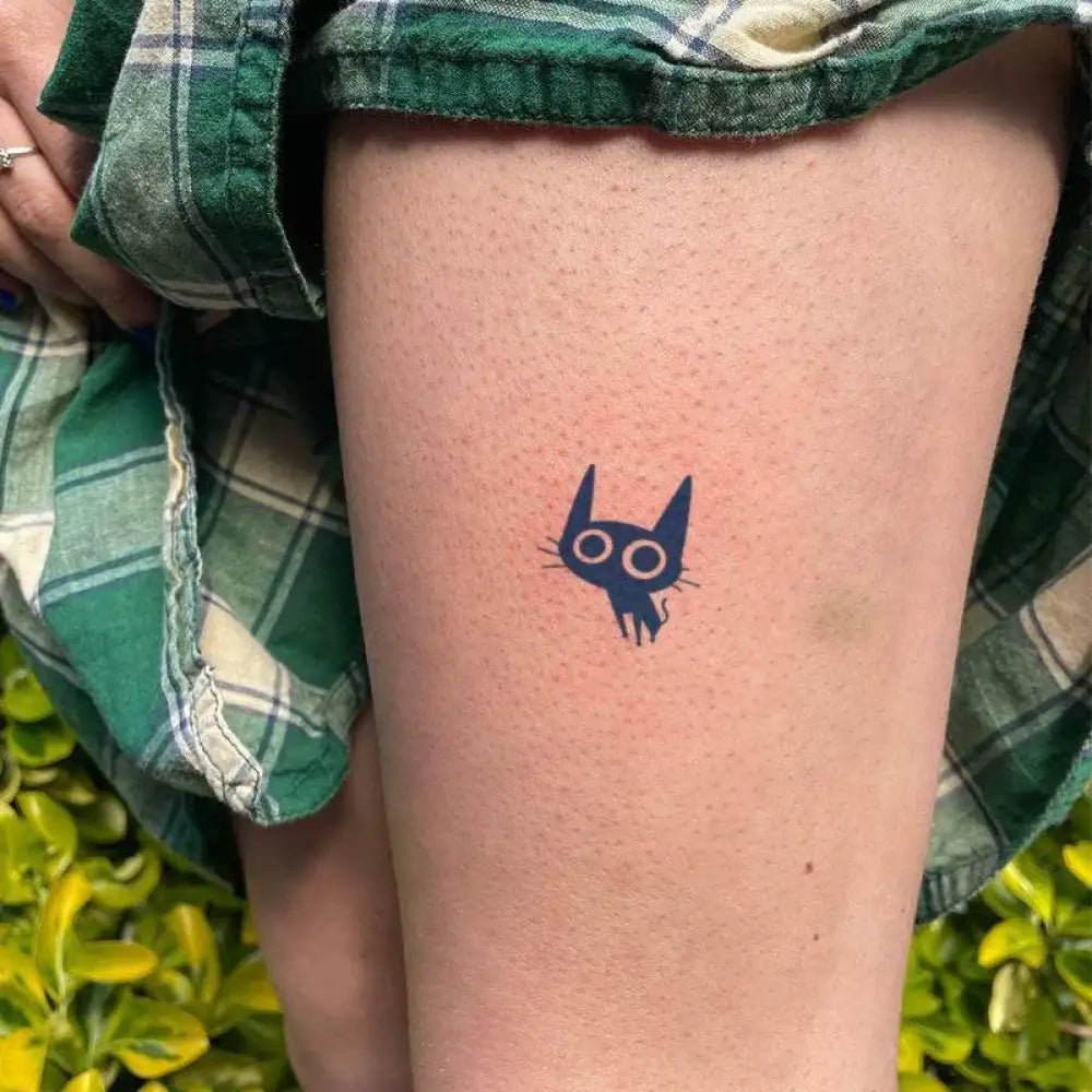 Person’s leg featuring a coal ball cat tattoo with luminous eyes from the Coal Ball Cat Collection