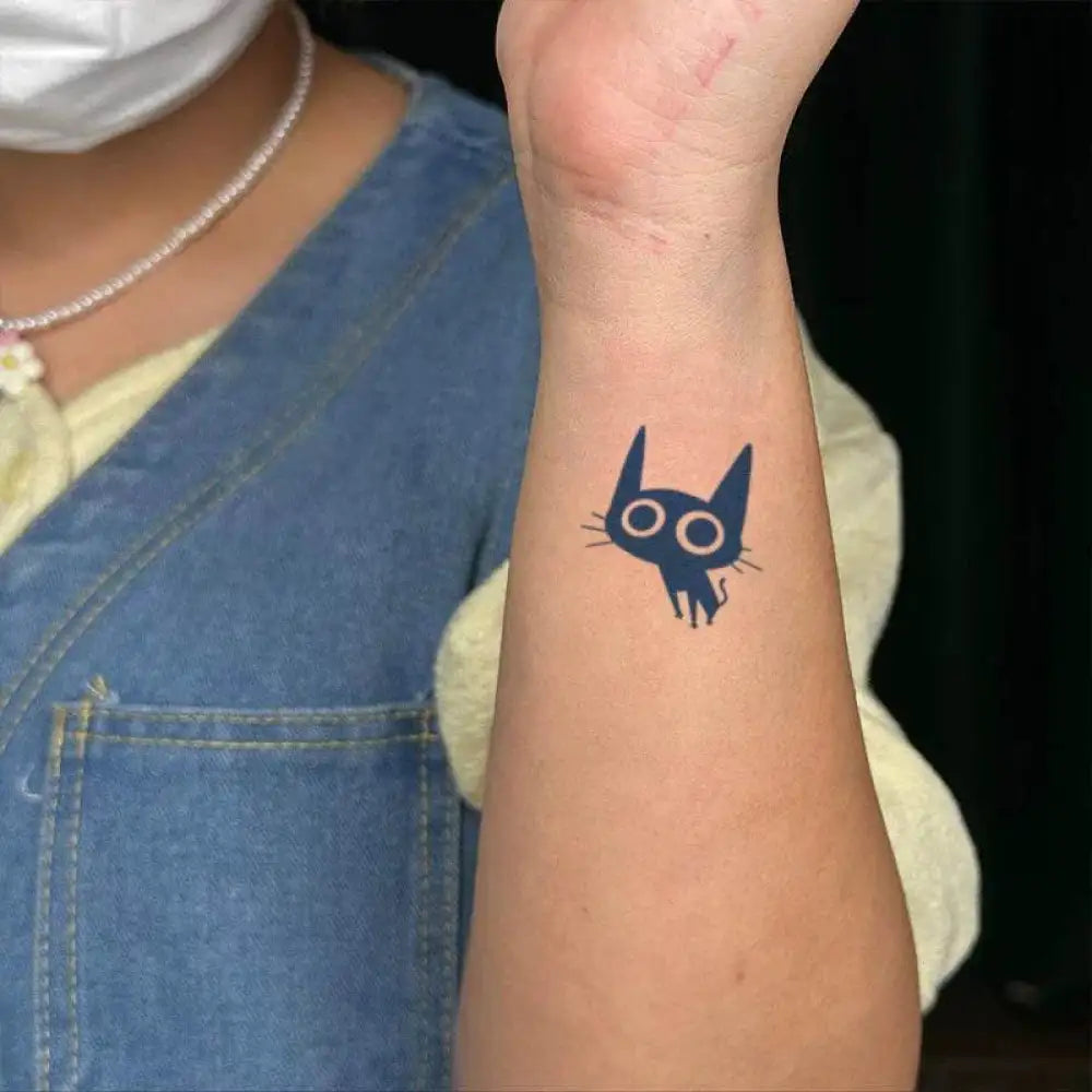 Black cat tattoo with luminous white eyes from the Coal Ball Cat Collection on arm