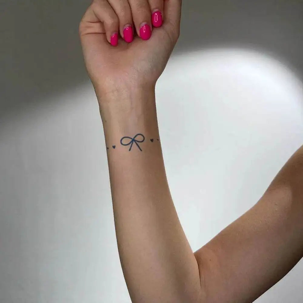 Delicate symmetrical bow tattoo sticker with hearts on person’s forearm and wrist