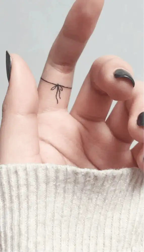 Hand with a black bow tattoo sticker on middle finger and dark nail polish, showcasing advanced hand-drawn design