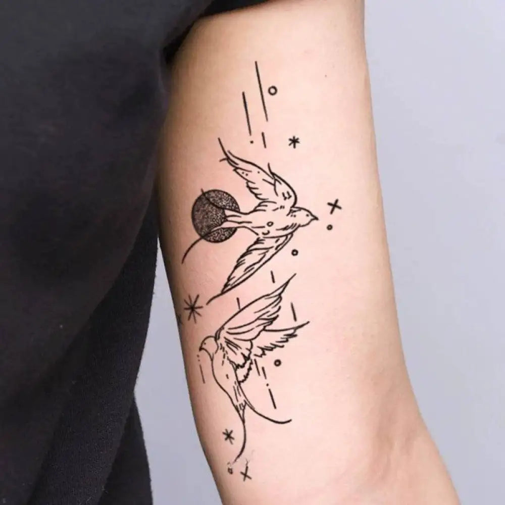 Minimalist tattoo of two flying birds and celestial elements on arm, perfect for happy flying birds enthusiasts